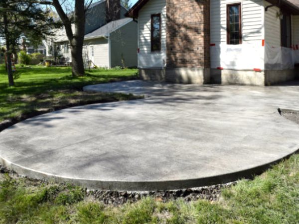 Curved concrete patio with saw-cut joints behind an older brick house