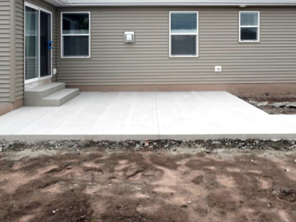 New concrete patio and poured steps behind a house with gray siding