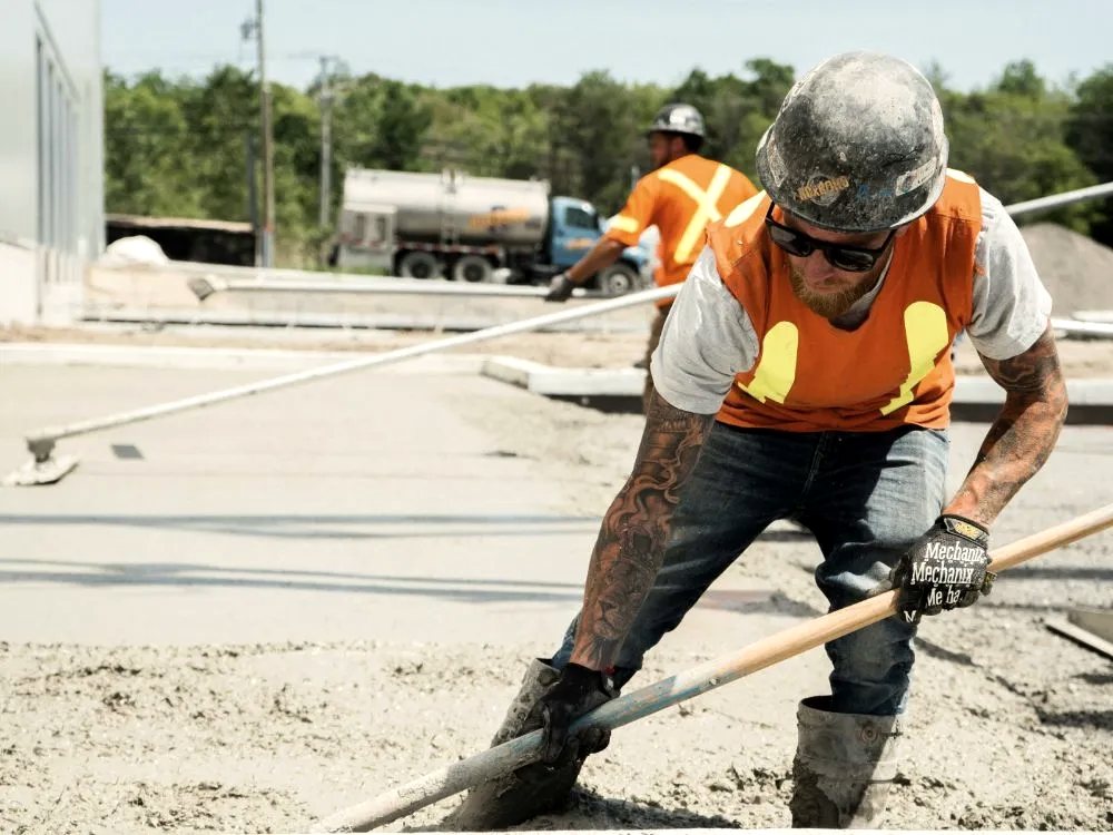 Concrete worker in a hard hat raking fresh concrete out to the forms